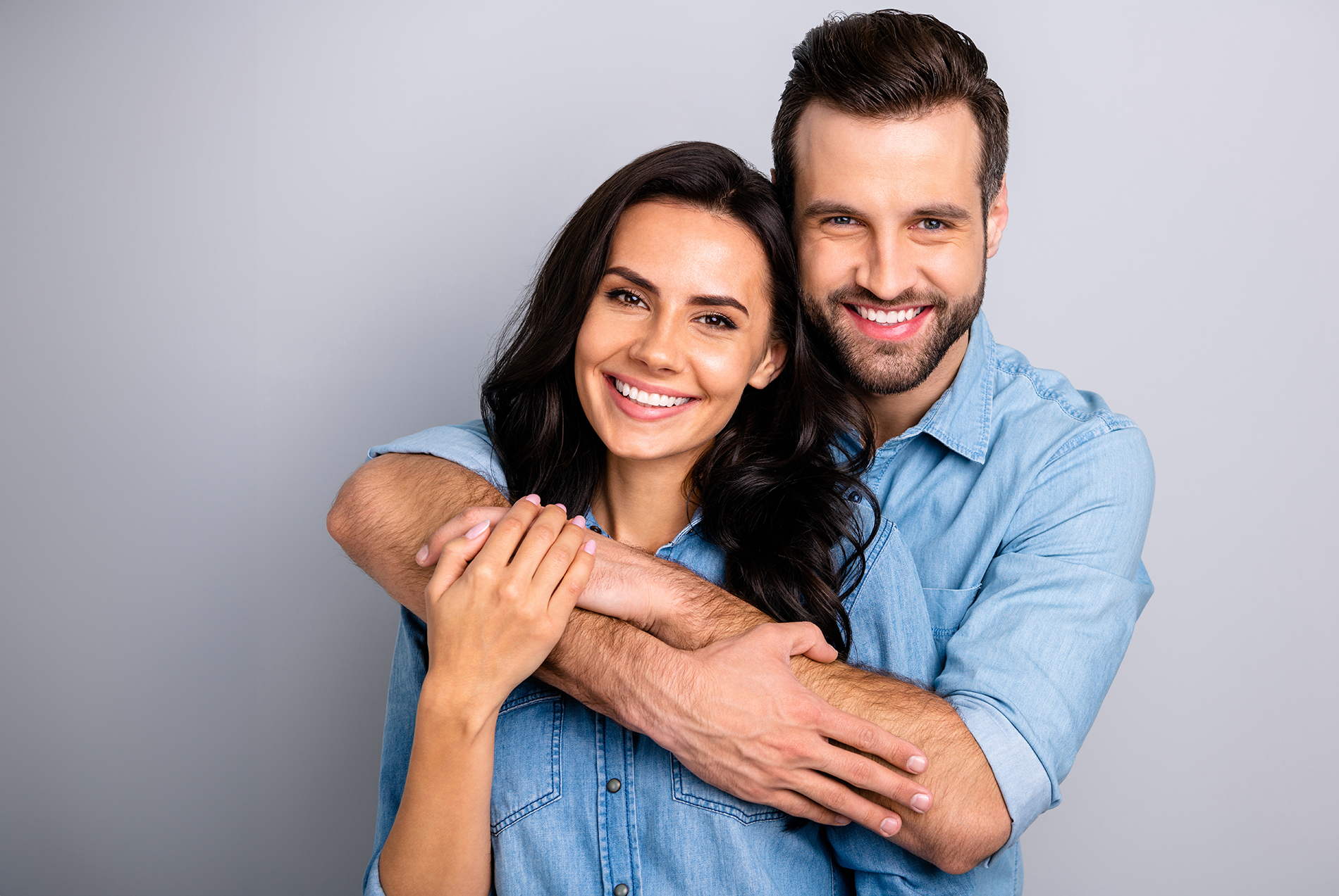 A man and a woman embrace in a studio portrait, both smiling.