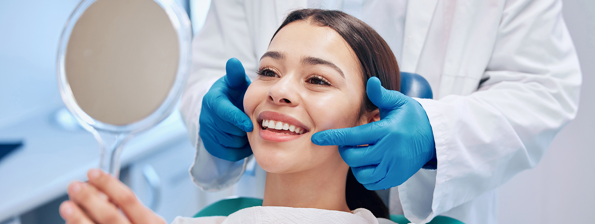 The image shows a person sitting in a dental chair with a smile, receiving dental care from a professional wearing protective gloves and a mask.