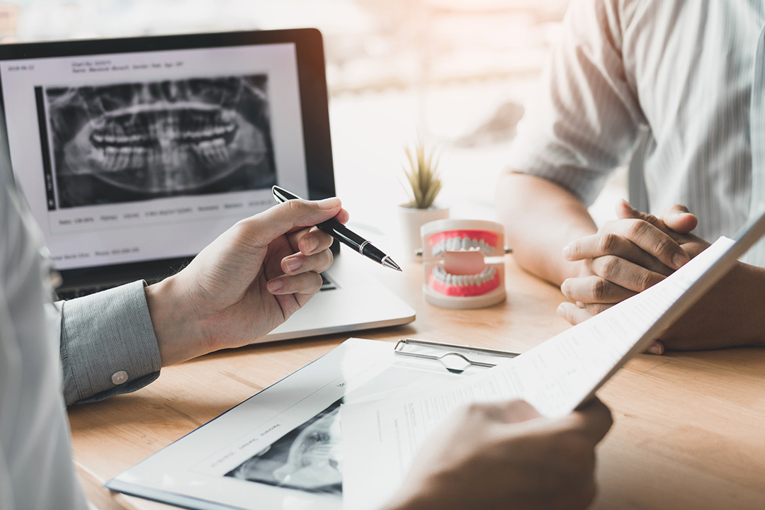 The image is a split photograph showing two different scenes. On the left side, there s a medical professional in a dental office examining a patient s mouth with a mirror and a light, while on the right side, a business meeting is taking place with a person writing on a tablet and another reviewing documents.