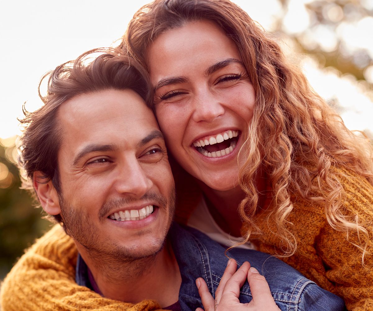A man and a woman are smiling and embracing each other, with the man wearing a yellow shirt.