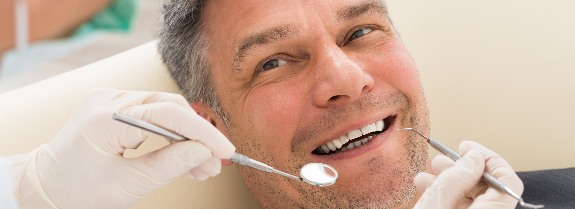 A man in a chair receiving dental care, with a smiling expression and a dentist performing the procedure.