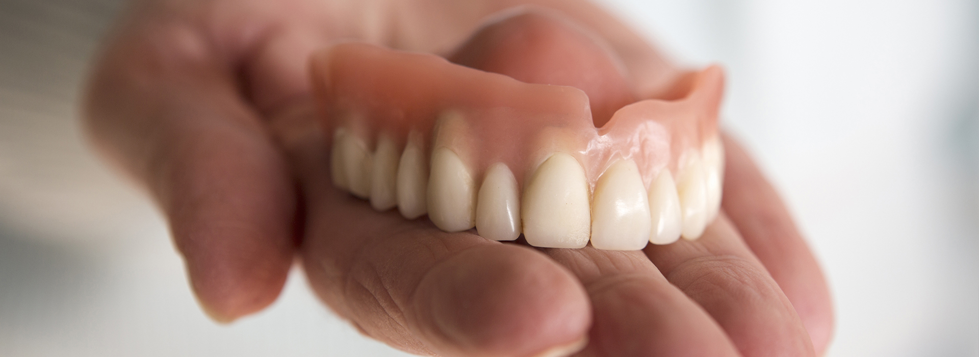 A human hand holding a set of artificial teeth, showcasing the prosthetic dental appliance.