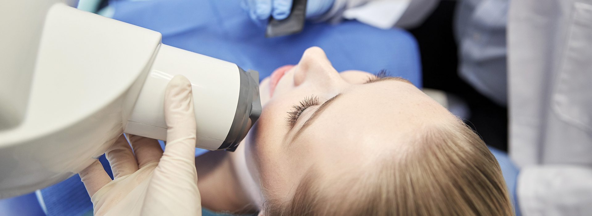 A woman receiving dental treatment, with a dentist using a magnifying device to examine her teeth, in an office setting.