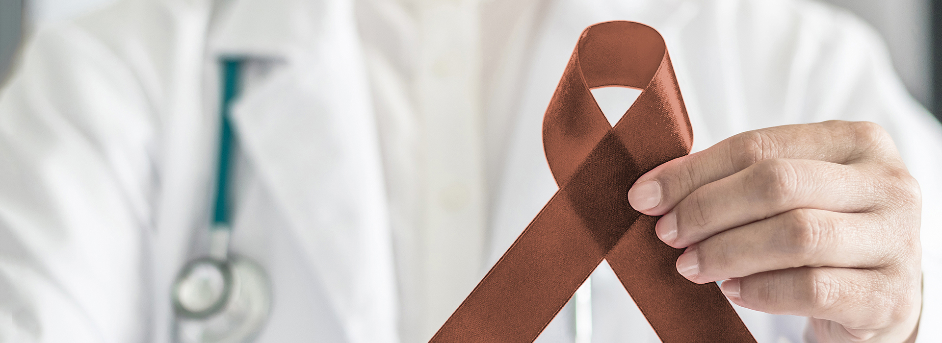 The image shows a healthcare professional wearing a white coat and holding a red ribbon with a symbol on it, standing in front of a background that is not clearly visible.