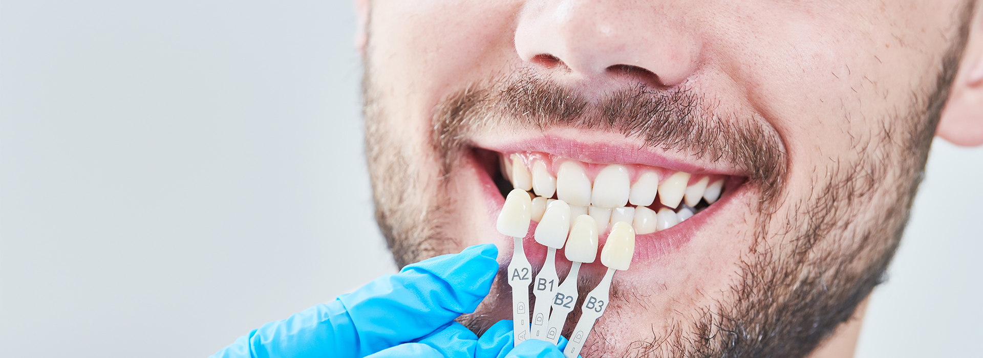 The image shows a man smiling with a dental implant, wearing blue gloves and holding a dental tool.