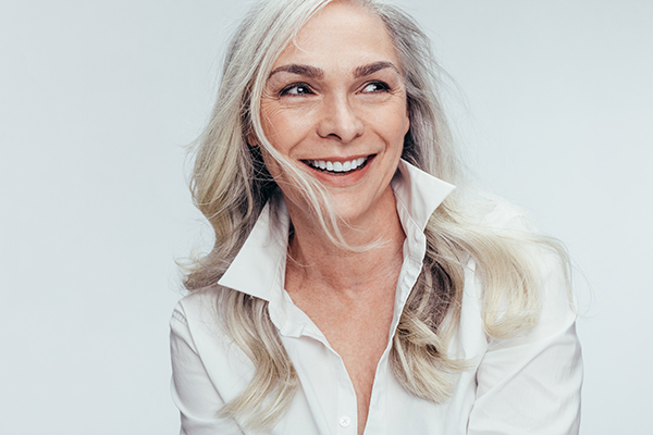 This is a portrait of a woman with short hair, wearing a white top and smiling at the camera.